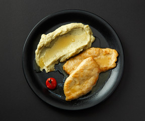 Mashed potatoes with chicken steaks on a black plate isolated on a black background