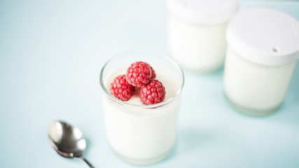 Open jar with homemade yogurt and raspberries on a blue background next to closed jars