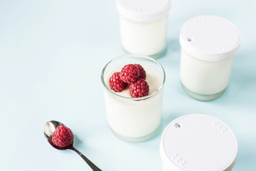 Open jar with homemade yogurt and raspberries on a blue background next to closed jars