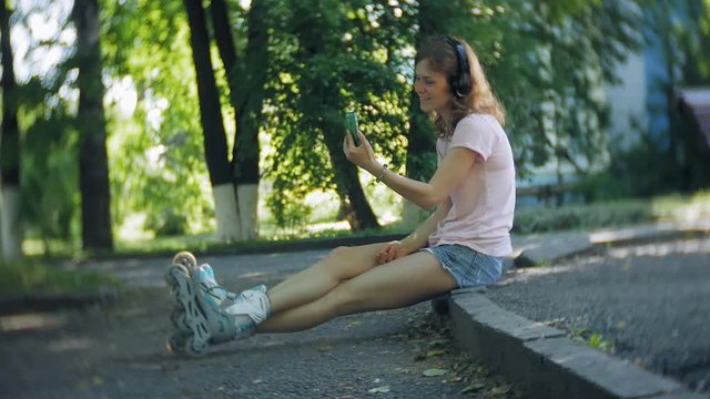 woman rollerblading and listening to music on headphones on the phone in the park