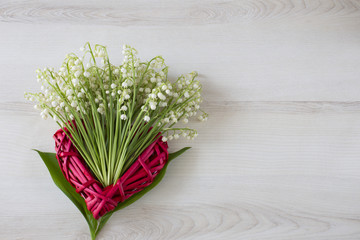 on a light background a red heart made of straw and a bouquet of lilies of the valley