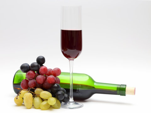 glass of red wine and bottle with grapes on a white background