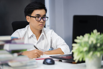 young man studying and writing on notebook with laptop