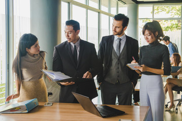 Executives and secretaries are discussing about the job information in a computer notebook.