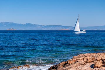 A sailboat passes near a rocky shore