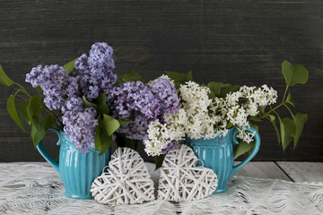 on a wooden table, two blue cups with a bouquet of lilac and two white wicker hearts