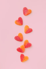 Heart shaped candy red and orange color on a pink background. Seven jelly candies viewed from above. Top view