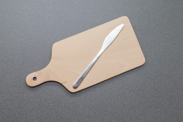 Holzbrettchen mit daraufliegendem silbernen Küchenmesser auf einer Arbeitsplatte in der Küche
