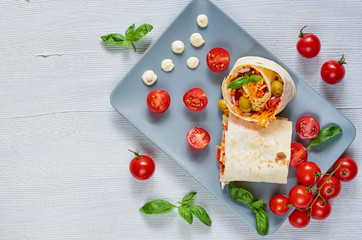 Shawarma sandwich or lavash with fresh vegetables and sauce on the gray plate decotated with cherry tomatoes, basil leaves. Traditional arabic food. Eastern cuisine. Top view with copy space for text