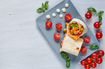 Shawarma sandwich or lavash bread with fresh vegetables and sauce on the gray plate decotated with cherry tomatoes, basil leaves. Traditional Turkish food. Eastern cuisine. Top view with copy space