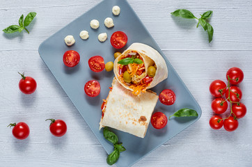 Naklejka na ściany i meble Shawarma sandwich or lavash snack with fresh vegetables on the gray plate decotated with cherry tomatoes, basil leaves, sauce on the gray concrete background. Traditional arabic food. Eastern cuisine