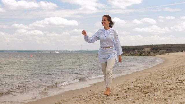 people and leisure concept - happy smiling woman walking along summer beach