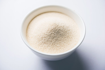 Raw unprepared semolina flour also known as Rava powder in Hindi in bowl or spoon. close-up...