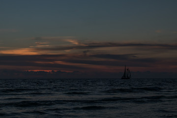 Silhouette of sailboat on the horizon at sunset on the beach