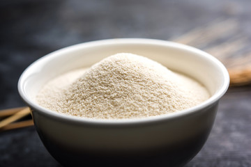 Raw unprepared semolina flour also known as Rava powder in Hindi in bowl or spoon. close-up isolated on white or moody background. selective focus