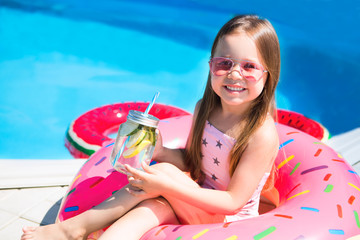 Little boy girl sits on a rubber ring and drinks lemonade about the pool, having fun in swimming pool.