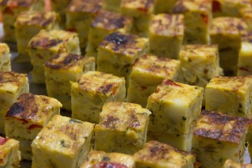 Close up on cubes of traditional Spanish potato omelette with red pepper. Snack party concept