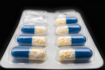 Packaging of blue tablets with white and yellow granules on a black background