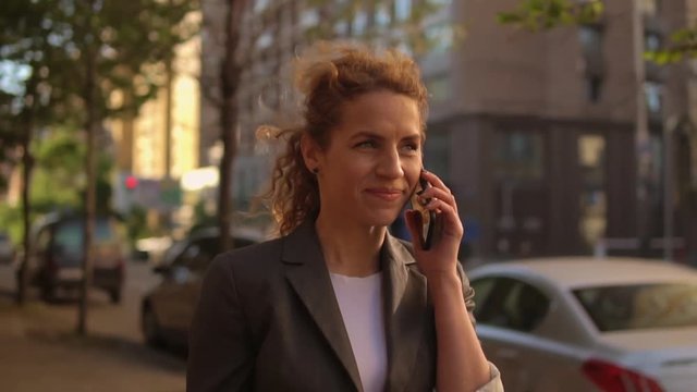 Beautiful woman is speaking on the phone. She wears grey suit.