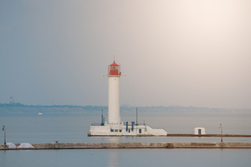 Summer seascape with a white lighthouse with red top in the middle. Calm sunny day