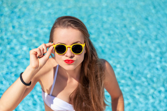Summertime in pool. Young woman with yellow sunglasses in pool.