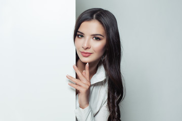 Beautiful brunette woman showing white empty blank paper banner background. Advertising marketing, business and education concept.