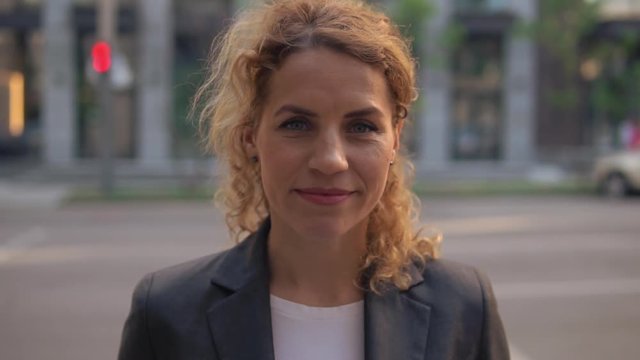 Blonde haired businesswoman standing in a busy street. female smiles calmly.