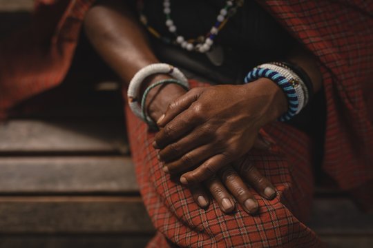Midsection of Maasai woman in traditional clothing sitting on bench