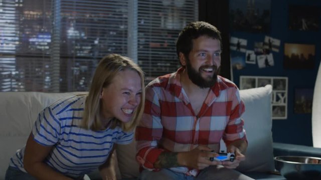 Couple chilling on sofa with gamepad and man mocking on girlfriend when winning videogame round and having fun