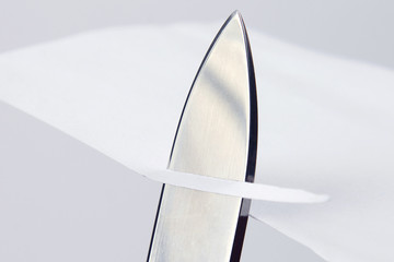 blade of a sharp knife cut across the white paper