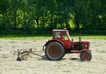 Naklejka premium Brahmenau / Germany: Old but robust red tractor from socialist times with rotary hay tedder on a small field in June