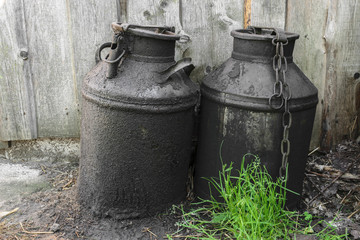 Black and oiled metal canisters in the countryside. Wooden wall in background