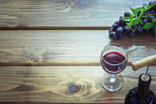 Open bottle of red wine with wineglass, corkscrew and ripe grape on wooden board. Copy space and top view.