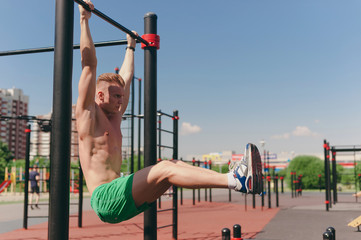 A young guy on a street Playground is pulled up on the bar - 212794426