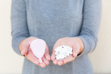 Tablets or Menstrual cup? Menstrual mug and tablets holds a female hand.