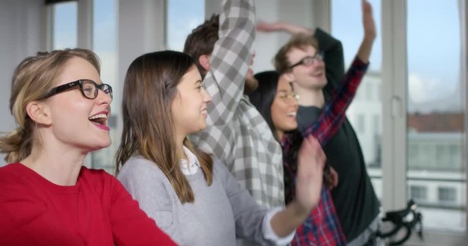 Five good mooded people in a modern office doing a la ola wave together
