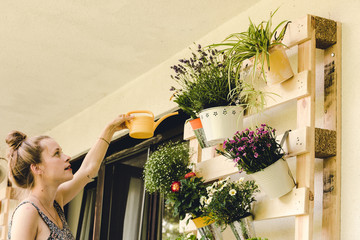 beautiful young woman watering her potted plants on the balcony - obrazy, fototapety, plakaty
