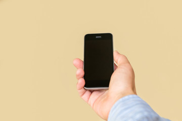 Mobile phone with blank black screen in a man's hand, isolated on a beige background