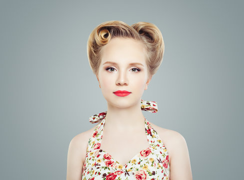 Young Blonde Woman with Vintage Retro Pinup Hairstyle and Makeup against Gray Wall Background