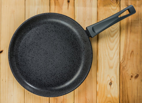 Cast-iron frying pan with non-stick coating against a background of a woody texture.