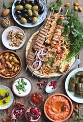 
    Middle eastern, arabic or mediterranean dinner table with grilled lamb kebab, chicken skewers with roasted vegetables and appetizers variety serving on wooden outdoor table. Overhead view.  - obrazy, fototapety, plakaty