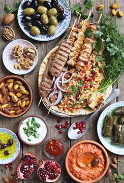 
    Middle eastern, arabic or mediterranean dinner table with grilled lamb kebab, chicken skewers with roasted vegetables and appetizers variety serving on wooden outdoor table. Overhead view. 