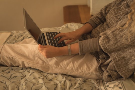 Midsection of woman using laptop while relaxing on bed at home