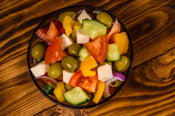 Glass bowl with greek salad on wooden table. Top view