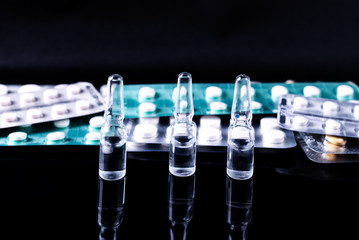 Ampoules and pills in a blister on a black background with reflection