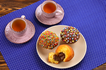 Baking with tea and chocolate on the table.  Two cups of tea with cupcakes and chocolate with a multicolored powder on the table.