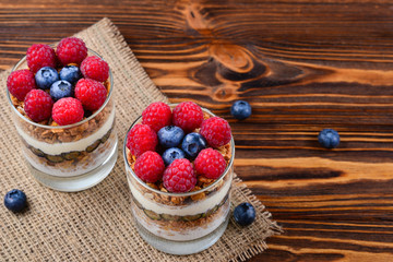 Healthy blueberry and raspberry parfait in a glass on a rustic brown wood background. Two portions. Space for text or design.