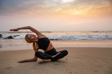 Fototapeta na wymiar Middle age woman in black doing yoga on sand beach