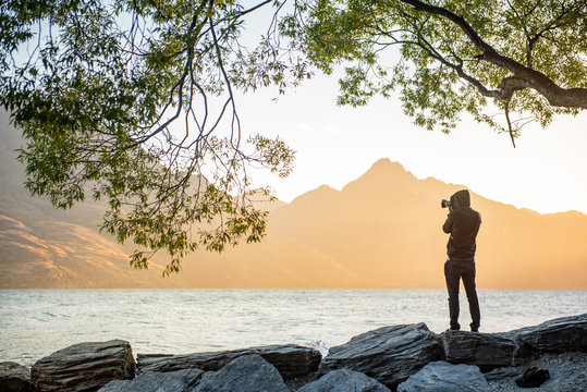 Young male photographer looking at scenery of Lake Wakatipu during golden hour sunset in Queenstown, South island, New Zealand, travel and landscape photography concepts