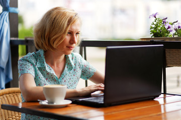 Woman is sitting at the table with a laptop and a cup of coffee